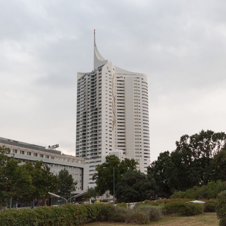 Tall white tower block with a curved crest beside trees