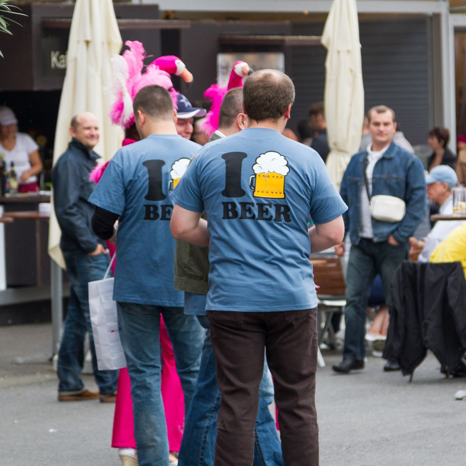 Backs of men in matching beer T-shirts at an outdoor café