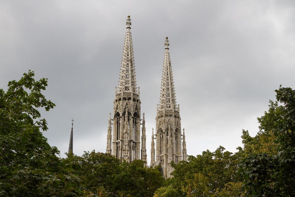 Twin Gothic church spires above green trees under dark clouds