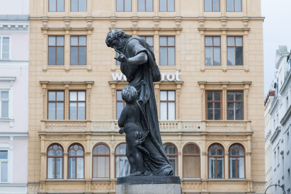 Bronze man bending toward a child in front of a cream building