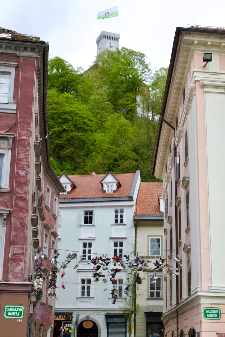 Narrow street with a pink facade and the green castle hill above