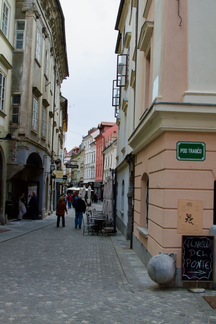 Narrow cobbled street with shops and a café board