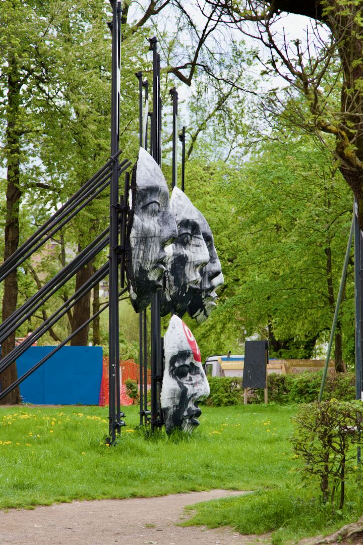 Sculpture of large faces hung on a metal frame in a park