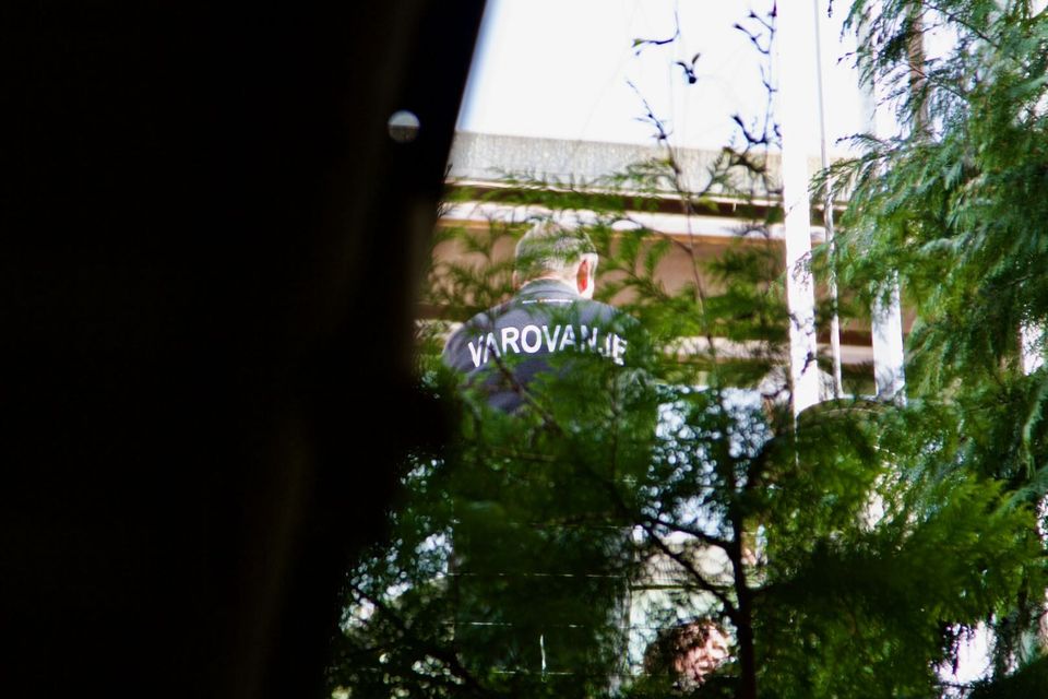 Security guard in a VAROVANJE jacket glimpsed through trees
