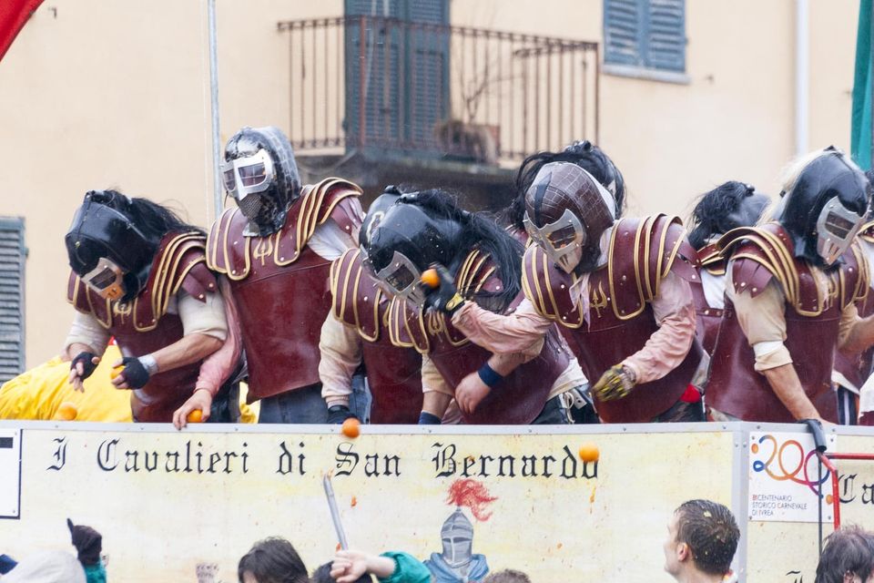 Masked orange throwers in armour and helmets lined up along a cart