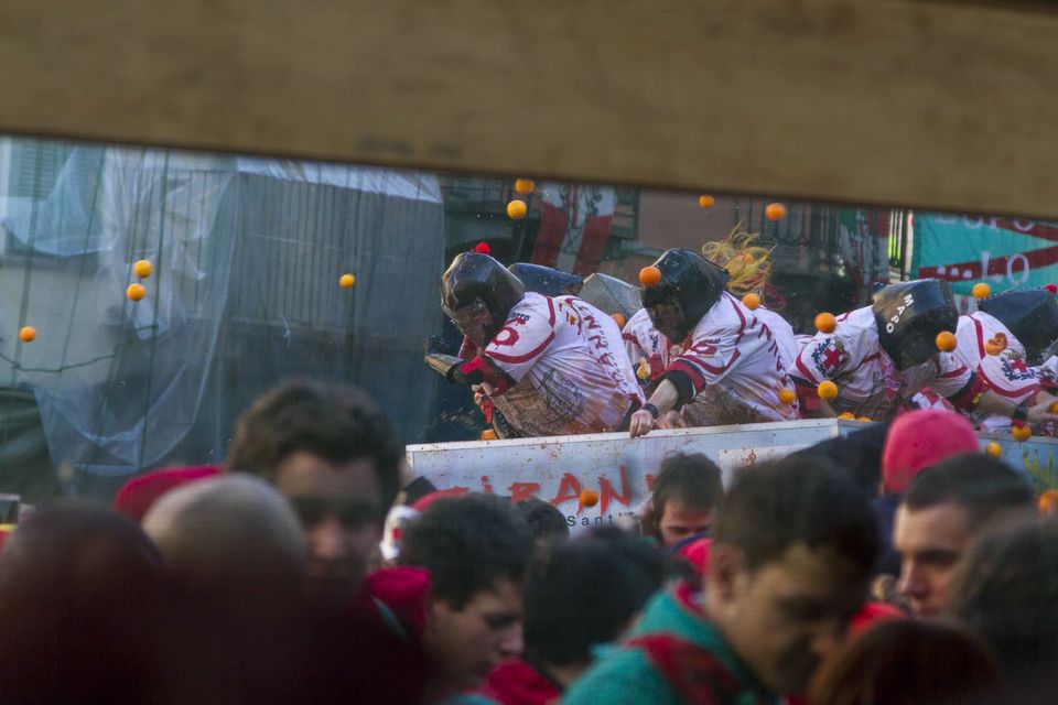 Masked throwers on a cart seen through a wooden frame, oranges flying