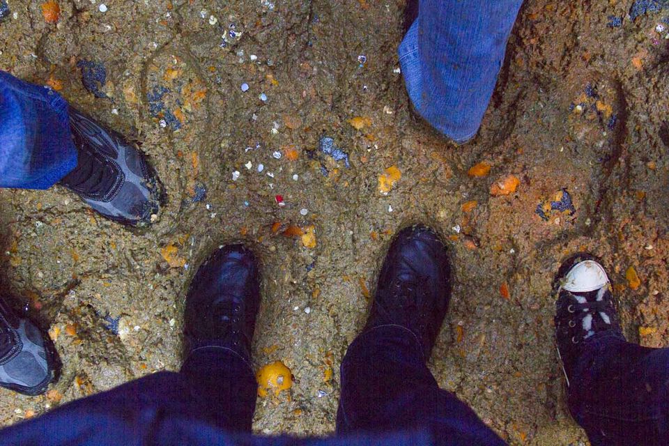 Muddy ground strewn with orange peel between several pairs of shoes