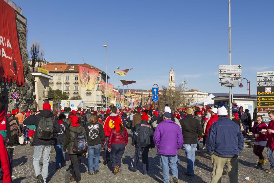 Crowd of red caps crossing a square, a bell tower beyond