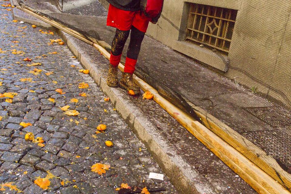 Cobblestone street littered with crushed oranges beside a gutter