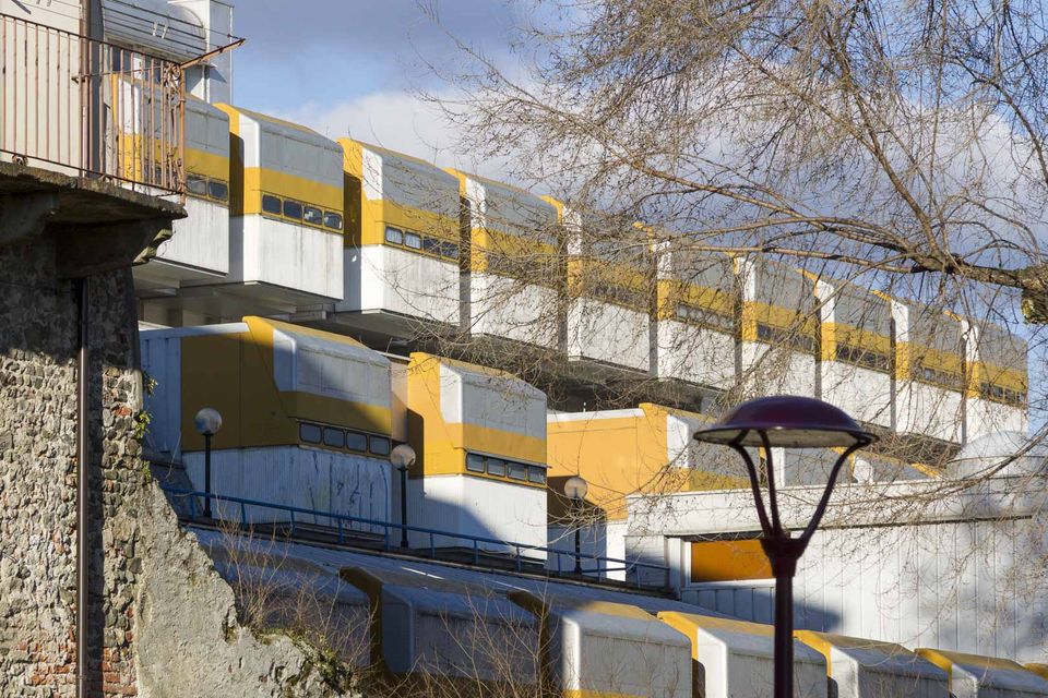 Terraced yellow and white modernist housing behind bare branches and a lamp