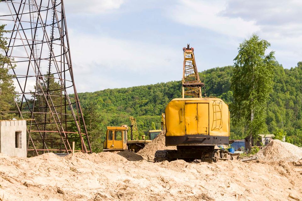 Yellow crane on a sand heap near the tower with wooded hills behind