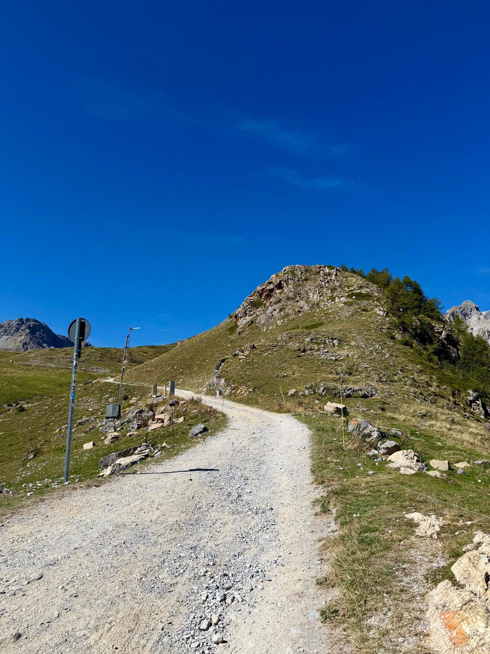 Gravel track curving up a grassy ridge past marker poles