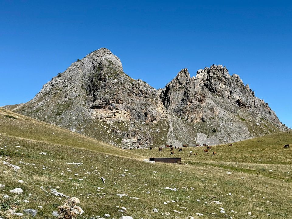 Two craggy peaks above a meadow and a low stone hut
