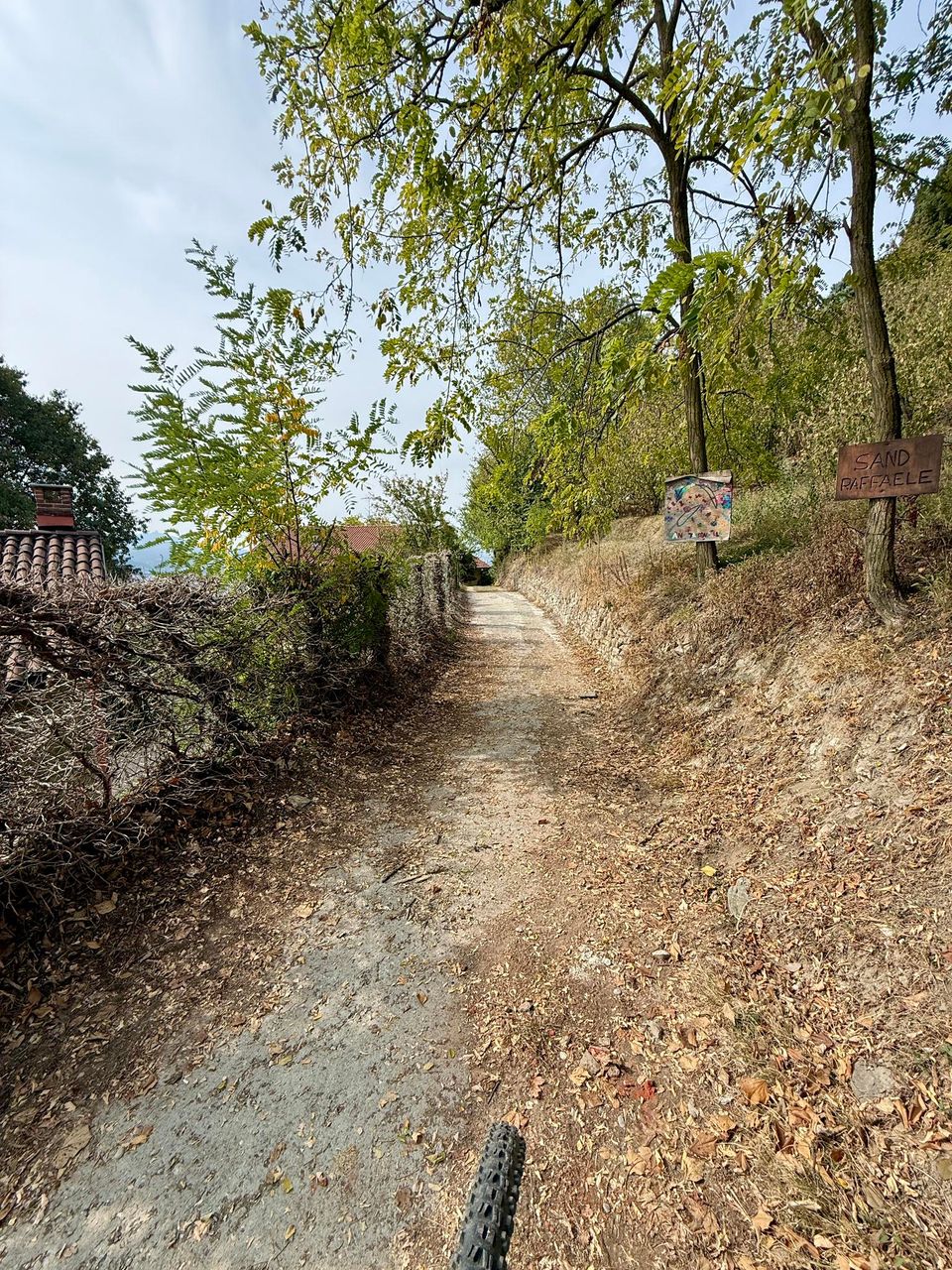 Dirt lane past a house wall and a wooden sign